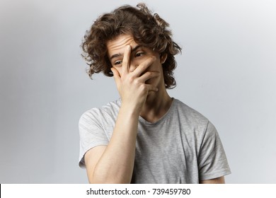 Stylish student guy with voluminous hair covering face with hand having frustrated look as he forgot about examination early in the morning. Handsome young man making face palm gesture in studio