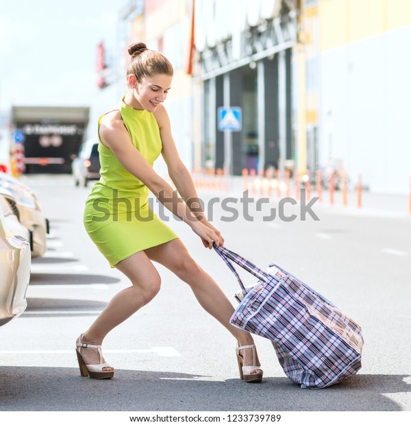 Stylish successful woman houls heavy big bag to car
trunk in summer day.