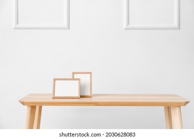 Stylish table with blank photo frames near light wall in room