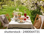 Stylish table setting with beautiful spring flowers, fruit drink and pie in garden