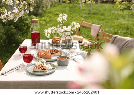 Stylish table setting with beautiful spring flowers, fruit drink and pie in garden
