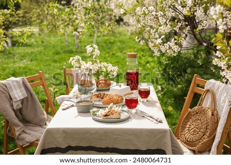 Stylish table setting with beautiful spring flowers, fruit drink and pie in garden