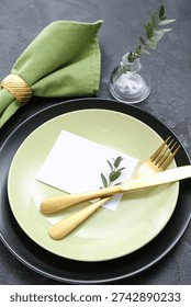 Stylish table setting with blank card and vase of plant branch on grunge black background