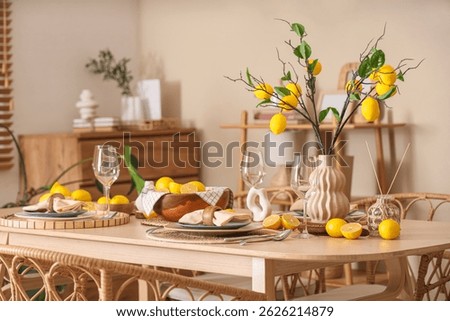 Stylish table setting decorated with many fresh citruses and beautiful lemon tree branches near beige wall in dining room