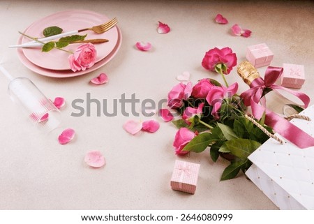 A stylish table setting featuring pink plates, fresh roses, a champagne bottle with a ribbon, and scattered rose petals.