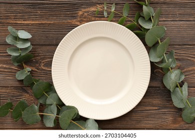 Stylish table setting with plate and eucalyptus branches on wooden background