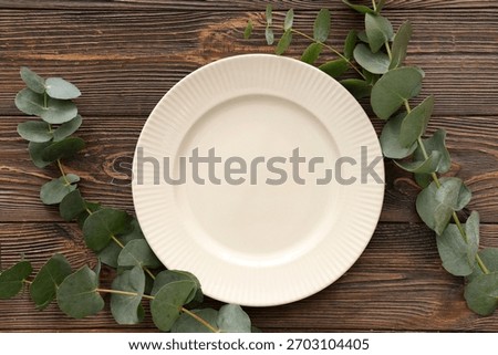 Stylish table setting with plate and eucalyptus branches on wooden background