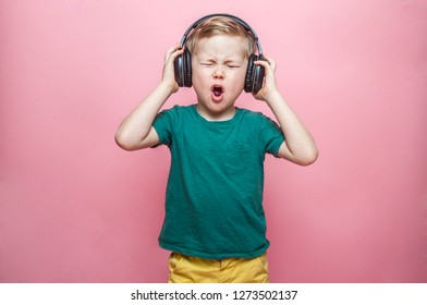 Stylish Teen Boy Listening Music In Headphones And Singing Against Pink Background. School Child Listening Loud Music In Wireless Earphones And Dancing. 