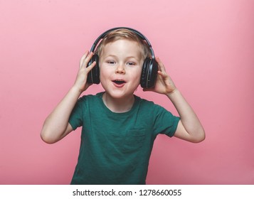 Stylish Teen Boy Listening Music In Headphones And Singing Against Pink Background. School Child Listening Loud Music In Wireless Earphones And Dancing