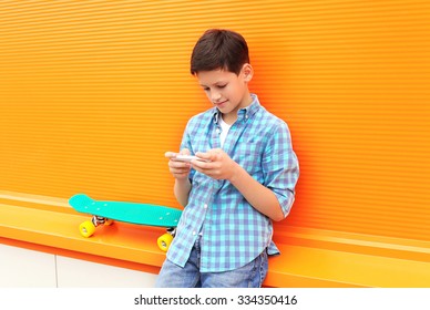 Stylish Teenager Boy With Skateboard Using Phone In City Over Orange Background