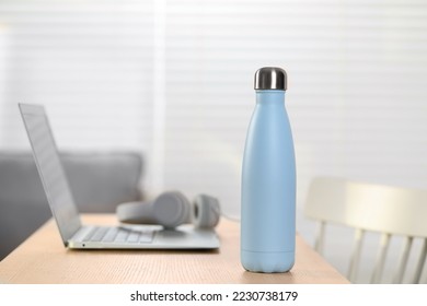 Stylish thermo bottle and laptop on wooden table at home. Space for text - Shutterstock ID 2230738179