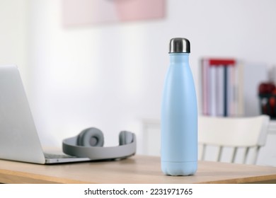 Stylish thermo bottle and laptop on wooden table at home. Space for text - Shutterstock ID 2231971765