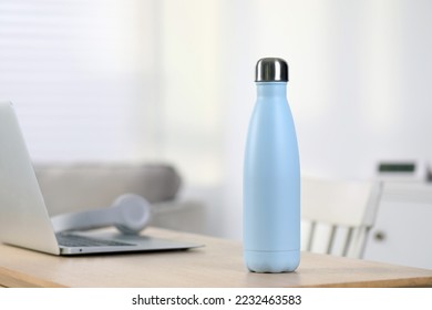 Stylish thermo bottle and laptop on wooden table at home. Space for text - Shutterstock ID 2232463583