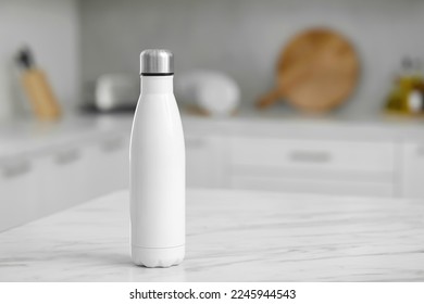 Stylish thermo bottle on white table in kitchen. Space for text