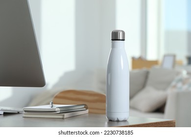Stylish thermo bottle on wooden table at workplace in office - Shutterstock ID 2230738185