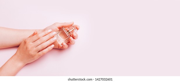 Stylish trendy female manicure. Woman's Hands holding perfume bottle on pink background. Top view, flat lay