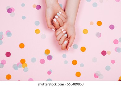 Stylish trendy female pink and blue manicure. Beautiful young woman's hands on pink pastel background with festive multicolored confetti.