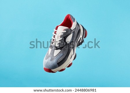 Stylish trendy sports shoes hanging on blue background. Men's fashion sport footwear. Air sneakers. Levitation concept. Flying colored leather sneakers isolated on a pastel background.