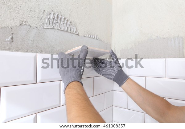 Stylish
trendy white ceramic tile with a chamfer on the kitchen wall. Tiler
hands in the process of laying white rectangular tiles on bathroom
wall.  Repair of apartments and bathrooms.
