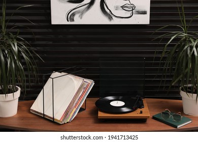 Stylish turntable with vinyl discs on table in room