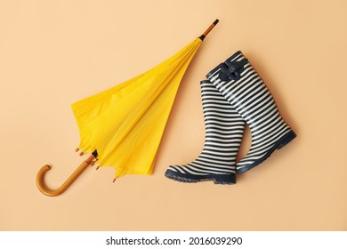 Stylish umbrella and rubber boots on color background