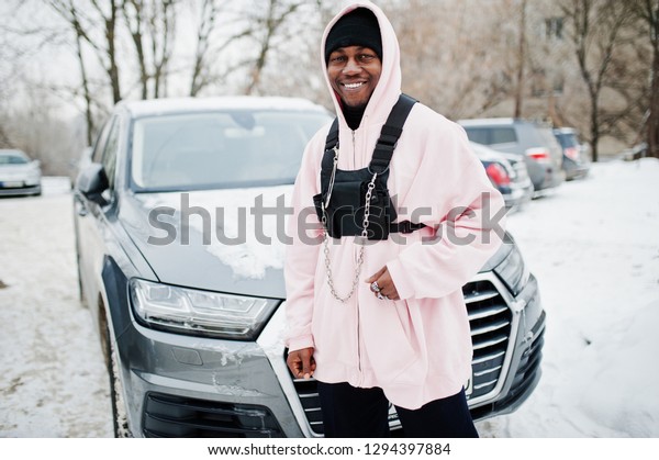 Stylish urban style\
african american man in pink hoodie posed against suv car at\
winter. Afro rapper\
guy.