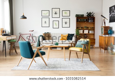 Stylish vintage furniture in a spacious flat interior with beige sofa, chairs and posters on the wall