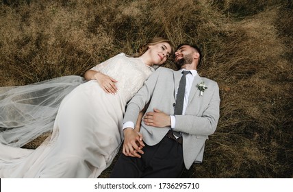 stylish wedding couple have a lot of fun and joy while enjoying the arms lying on the grass,wedding day of a young and beautiful couple,top view of the newlyweds who are lying,attractive couple