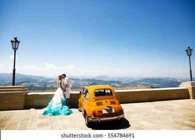 Elegante pareja de bodas besada antes del retro amarillo Fiat 500 con gran vista sobre las montañas detrás de ellos