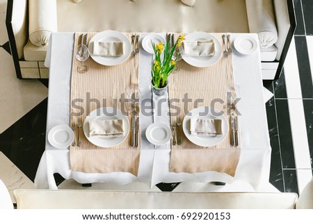 Stylish, white dining festive table and sofas. Minimalist interior in monochrome. Black and white concept. Wedding preparation. Empty restaurant top view. Close-up