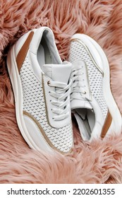 Stylish White Female Shoes On Pink Faux Fur Background, Copy Space. New Sneakers On The Rug, Close Up. Beauty And Fashion Concept. Flat Lay, Top View. Overhead Shot 