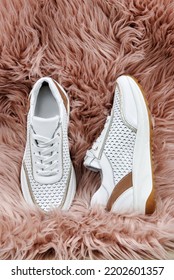 Stylish White Female Shoes On Pink Faux Fur Background, Copy Space. New Sneakers On The Rug, Close Up. Beauty And Fashion Concept. Flat Lay, Top View. Overhead Shot 