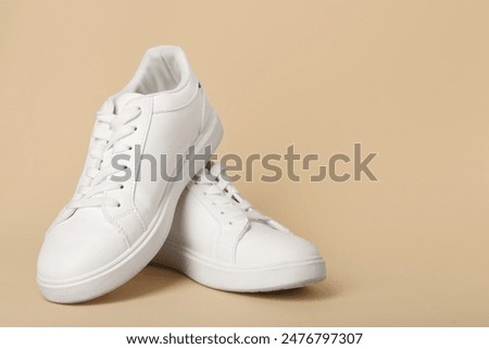 Stylish white sneakers on beige background