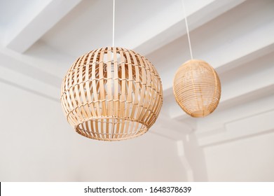 A stylish wicker wooden chandelier in boho and Bali style hangs on the ceiling near a white canopy made of weightless tulle. Part of the light airy interior.