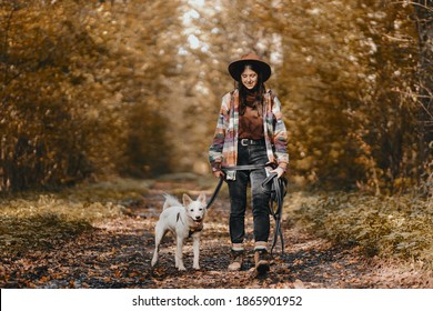 Stilvolle Frau mit Rucksack-Wanderung mit bezauberndem weißem Hund im sonnigen Herbstwald. Cute schweizer Hirtenwelpen und Eigentümerinnen reisen im Herbstwald. Textbereich