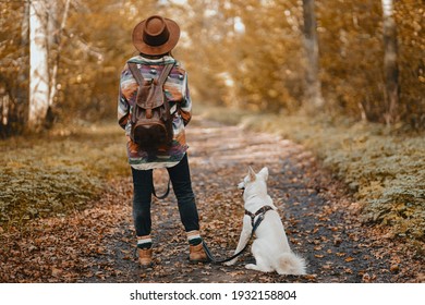 Stylish Woman With Backpack Hiking With Adorable White Dog In Sunny Autumn Woods. Cute Swiss Shepherd Puppy And Owner Female Traveling In Autumn Forest. Space For Text