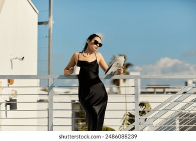 A stylish woman in a black slip dress and sunglasses enjoys a morning coffee while reading on the balcony of a Miami villa. - Powered by Shutterstock