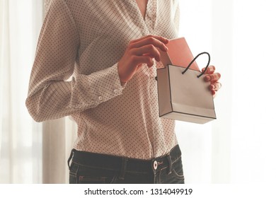 Stylish Woman In A Blouse Pulling A Box Of Favorite Perfumes Out Of A Gift Paper Bag. Receive Gifts From A Loved Ones 