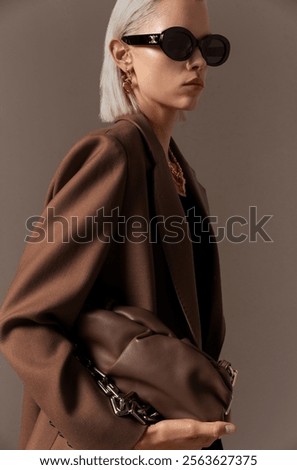 Stylish Woman in Brown Blazer and Sunglasses Holding Fashionable Leather Bag.