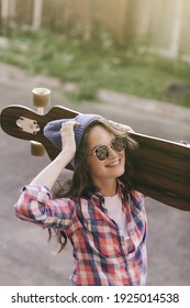 Stylish woman in checkered shirt in hat with longboard