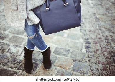 Stylish Woman With Crossed Legs In Blue Jeans And Big Leather Dark Blue Bag In Hand. Winter Fashion Outfit