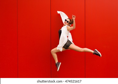 Stylish woman dancing and jumping on a street against a red wall - Shutterstock ID 474521617