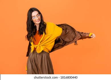 stylish woman in glasses and leather jacket standing with outstretched hand isolated on orange