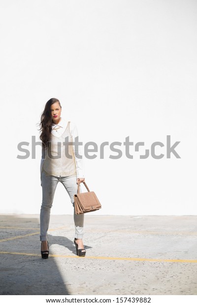 Stylish woman holding brown bag posing and looking\
at camera