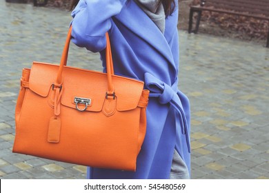 Stylish Woman In Light Blue Coat With Big Orange Handbag On The City Streets. Autumn Wardrobe. Street Look, Street Style.
