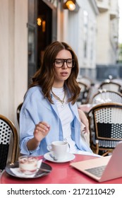 Stylish Woman Looking At Blurred Laptop Near Coffee And Dessert On Cafe Terrace In Paris