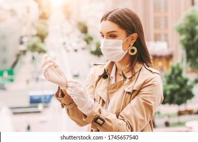 Stylish woman in medical face mask wear protective latex gloves on city street. Beautiful elegant hipster girl in protective face mask put on medical gloves outdoors. COVID-19 coronavirus protection
