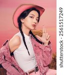 Stylish Woman in Pink Cowgirl Outfit with Braided Hair and Playful Pose Against Pastel Background.