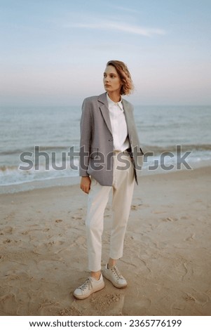Stylish woman posing on autumn beach in wild grass. A woman enjoys the autumn nature on the beach, relaxing. Fashion, style and relaxation concept.