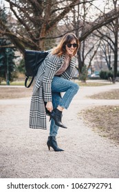 Stylish Woman Posing Outdoors, Zipping Up Her Black Ankle Boot. Brunette Fashion Blogger  In A Trendy Outfit, Houndstooth Pepita Pattern Coat, Vintage Mom Jeans And High Heel Shoes.